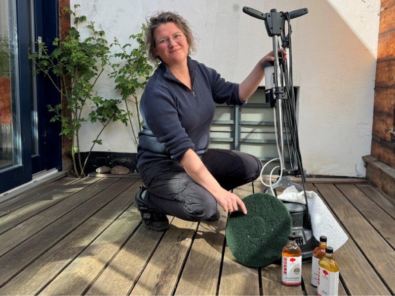 Frau mit Leinos-Floorboy und Reinigungs- und Pflegeprodukten auf einer Holzterrasse