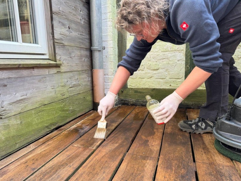 Frau ölt eine Holzterrasse und trägt das ökologische Leinos-Pflegeöl mit dem Pinsel auf